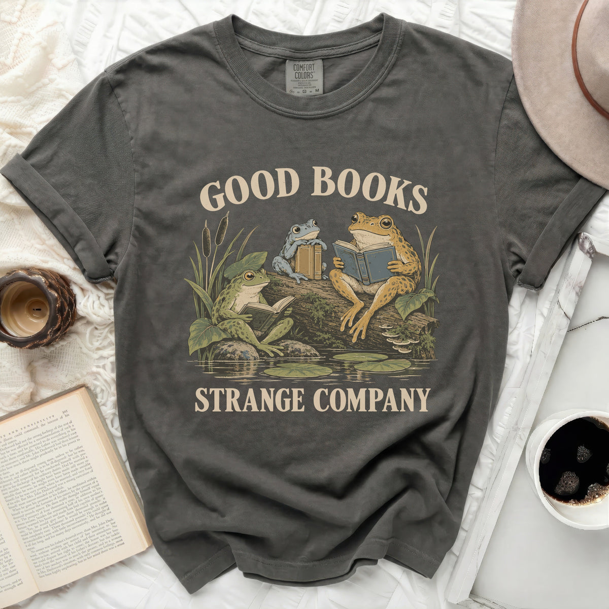 Dark grey t-shirt with a graphic of three frogs reading books with text "GOOD BOOKS STRANGE COMPANY".