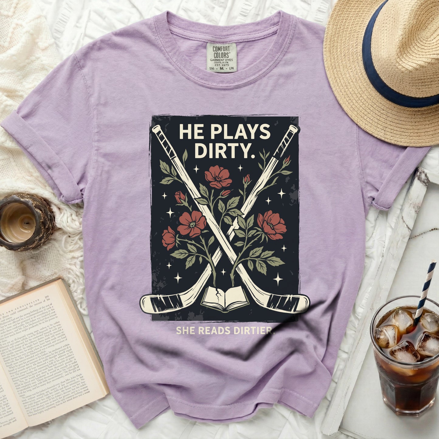Purple t-shirt with crossed hockey sticks and floral design, text HE PLAYS DIRTY. SHE READS DIRTIER.