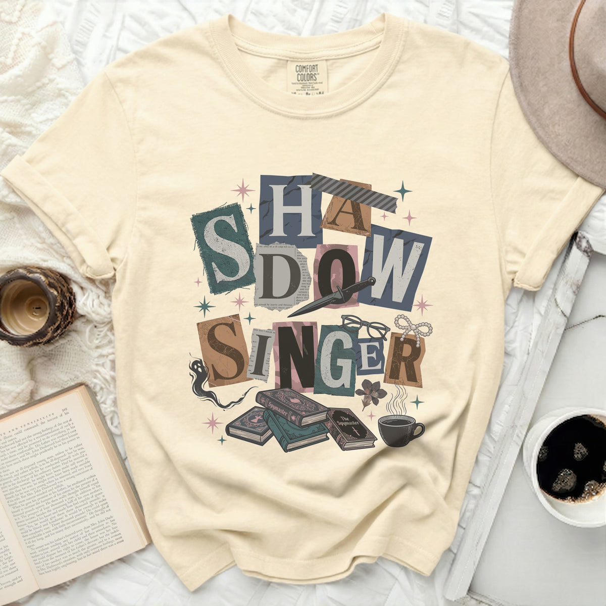 Cream t-shirt with "Shadow Singer" graphic, books, and coffee.