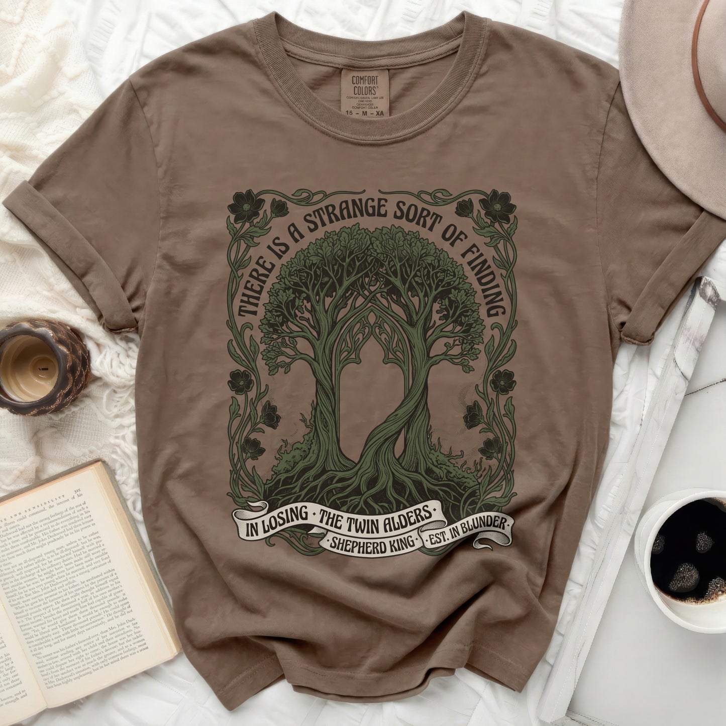 Brown t-shirt with trees and text "There is a strange sort of finding".