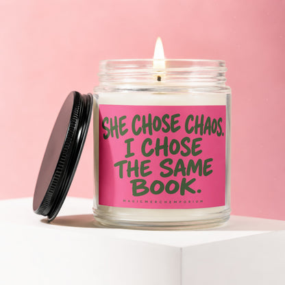 Lit candle in glass jar with pink label saying "SHE CHOSE CHAOS. I CHOSE THE SAME BOOK."