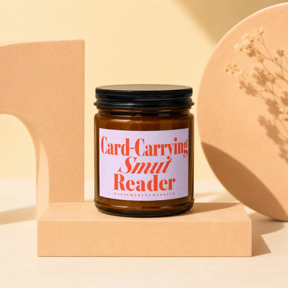 Brown glass candle with "Card-Carrying Smut Reader" label on display stand.