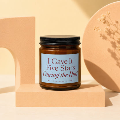 Brown glass candle with blue label reading "I Gave It Five Stars During the Hurt."