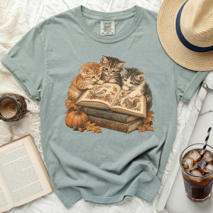 Three kittens read a book with a bird and squirrel, surrounded by autumn leaves and a pumpkin.