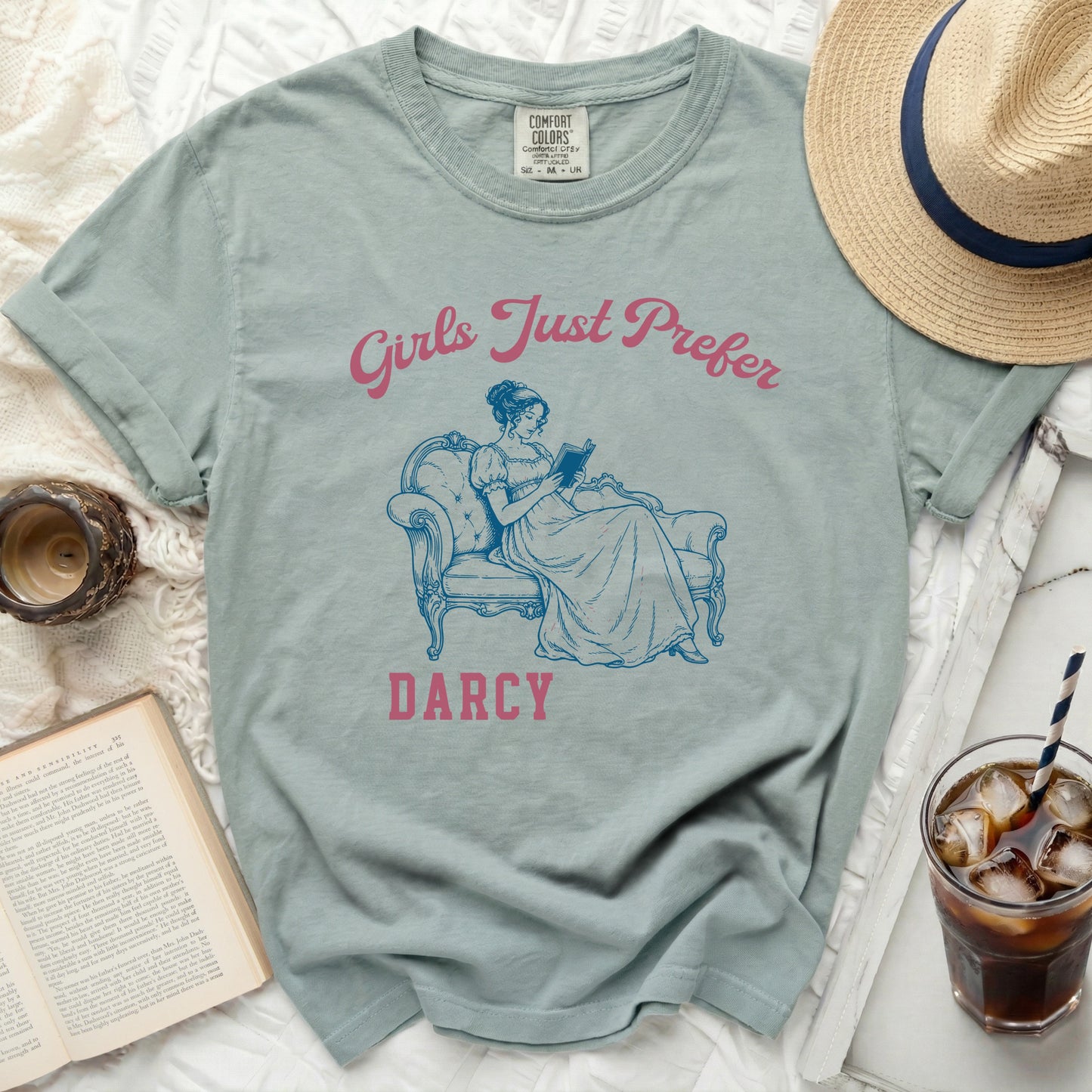 Light blue t-shirt with a graphic of a woman reading and text "Girls Just Prefer Darcy".