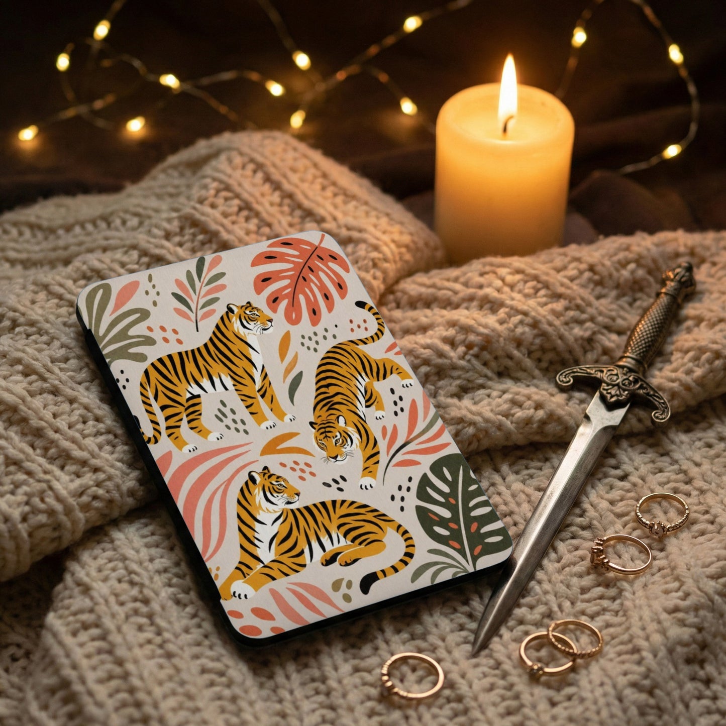 Phone case with tigers and tropical leaves on a knit blanket with candle and dagger.