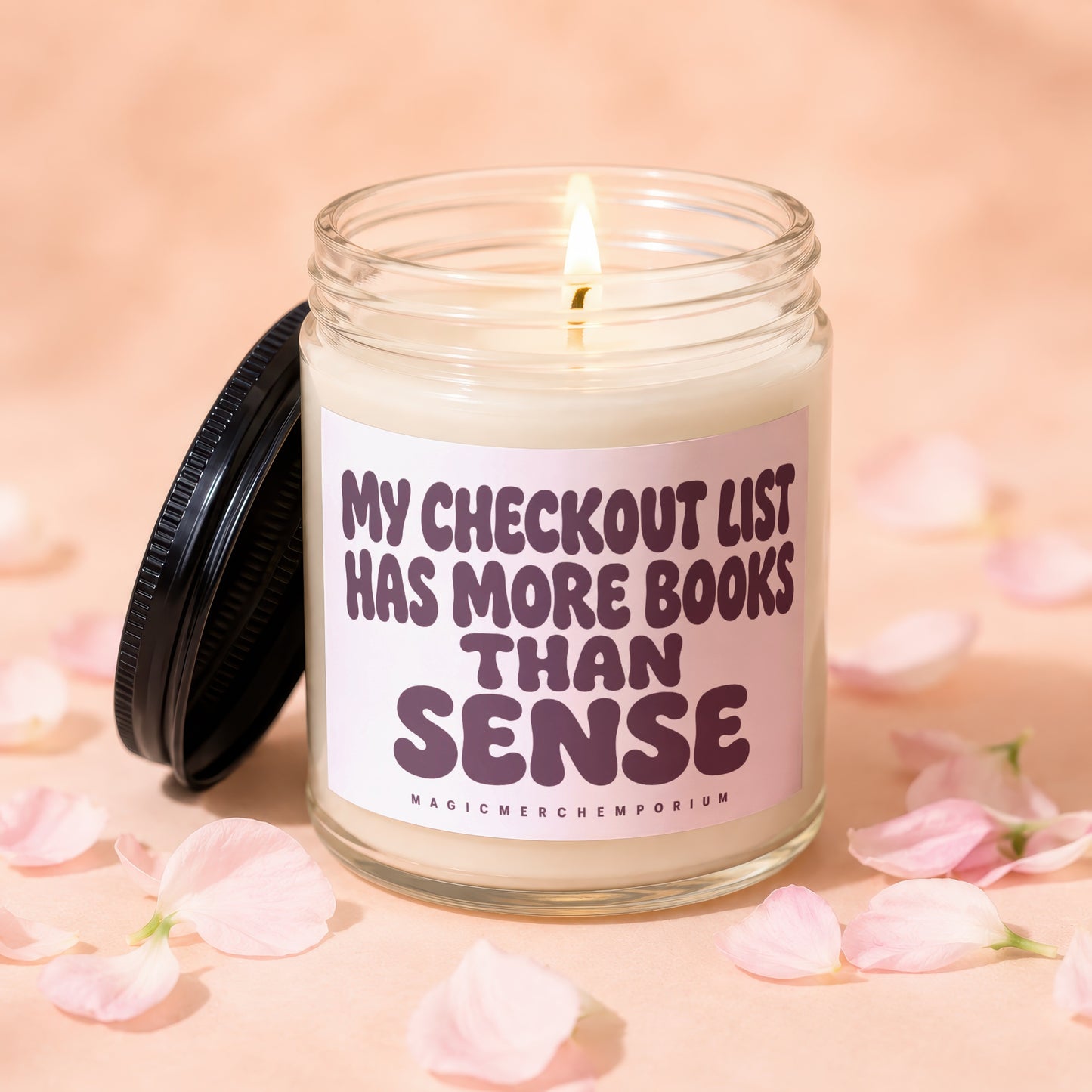 Jar candle with text "My checkout list has more books than sense" amidst pink petals.
