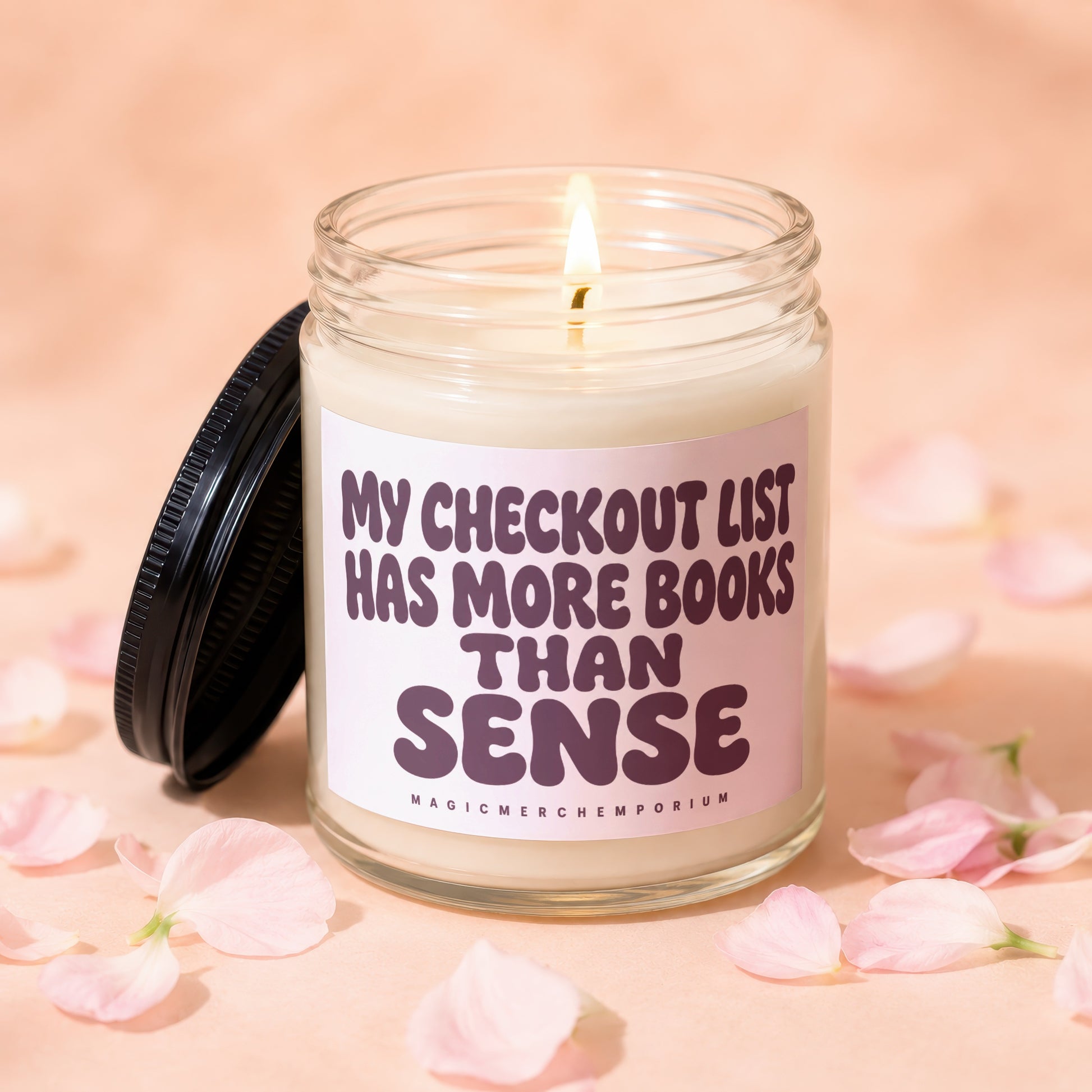 Jar candle with text "My checkout list has more books than sense" amidst pink petals.
