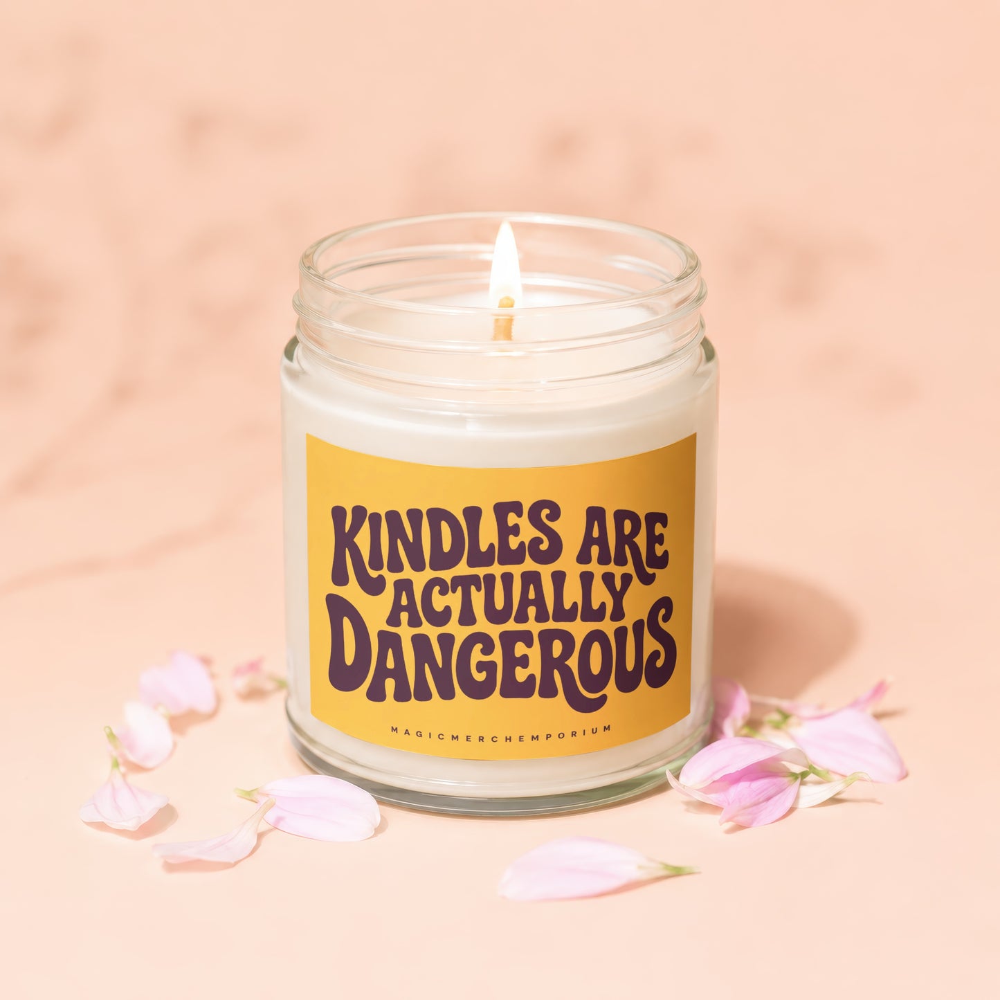 Candle with "Kindles are actually dangerous" text on yellow label, surrounded by pink petals.