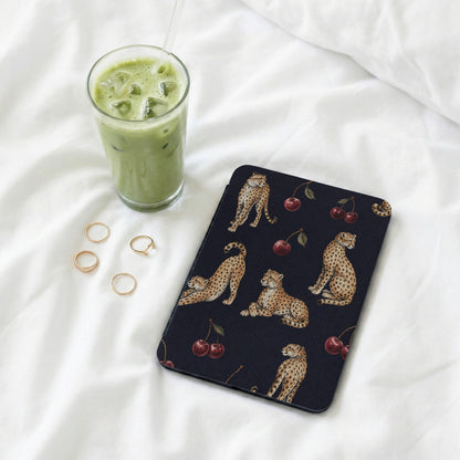 Dark case with leopard and cherry pattern, next to a green drink and rings.