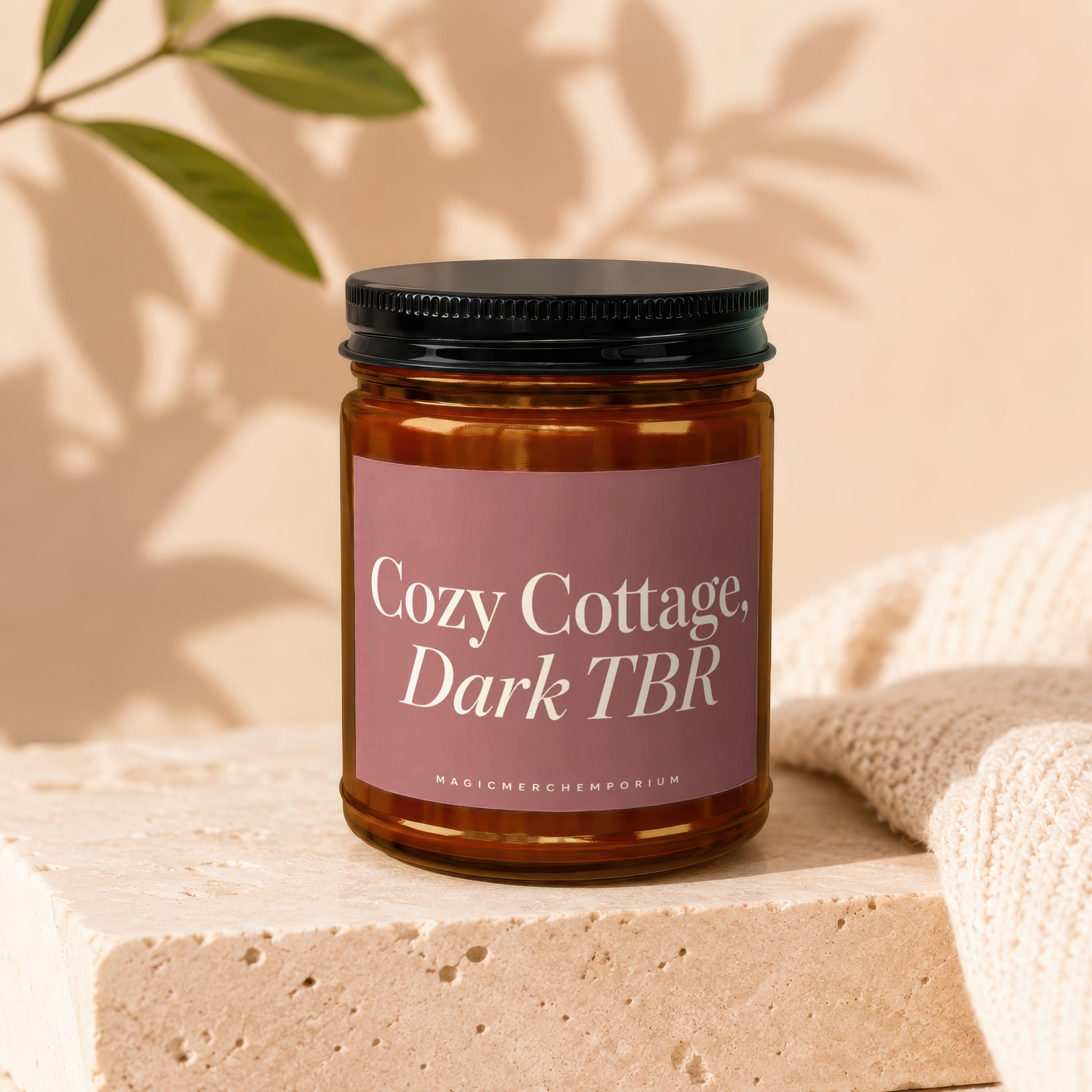 Amber glass candle with "Cozy Cottage, Dark TBR" label and "MAGICMERCH" on a stone block.