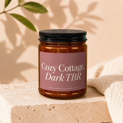 Amber glass candle with "Cozy Cottage, Dark TBR" label and "MAGICMERCH" on a stone block.