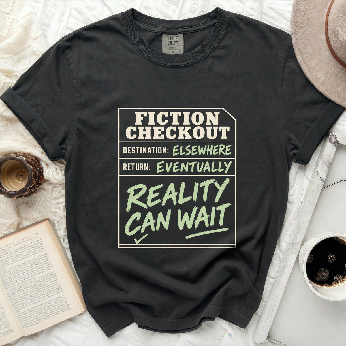 Dark t-shirt with "FICTION CHECKOUT DESTINATION: ELSEWHERE RETURN: EVENTUALLY REALITY CAN WAIT" text.