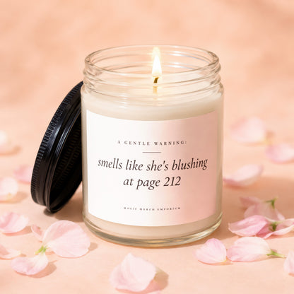 Glass candle with lit flame and lid off, reads "smells like she's blushing at page 212".