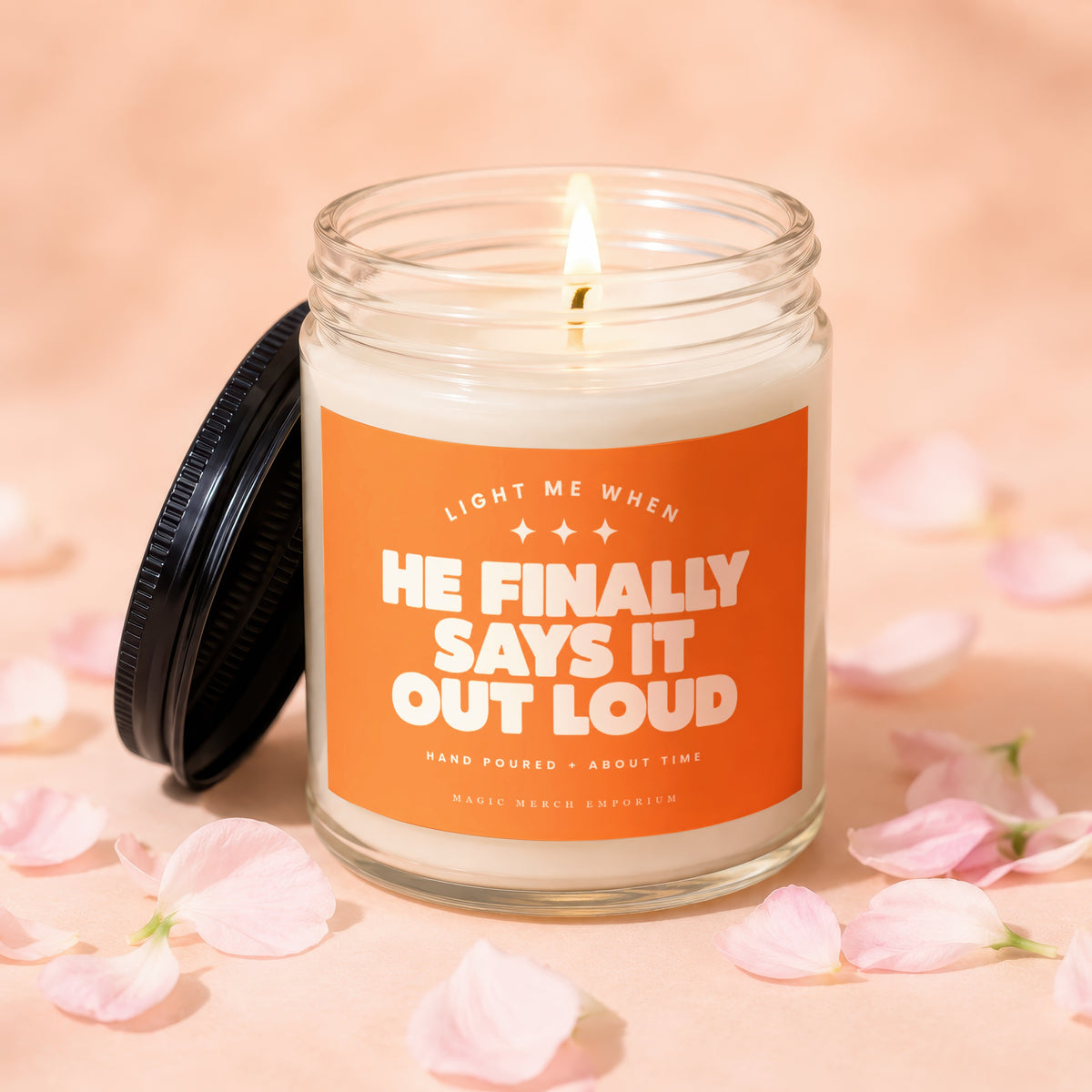 Glass jar candle with orange label reading "Light Me When He Finally Says It Out Loud"