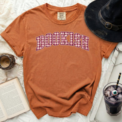 Orange t-shirt with "BOOKISH" in plaid lettering, styled with a book and drink.