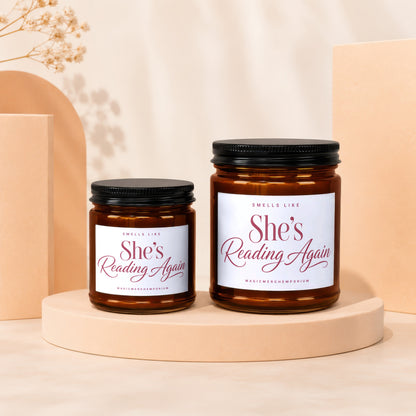 Two amber glass candles with white labels reading "She's Reading Again".