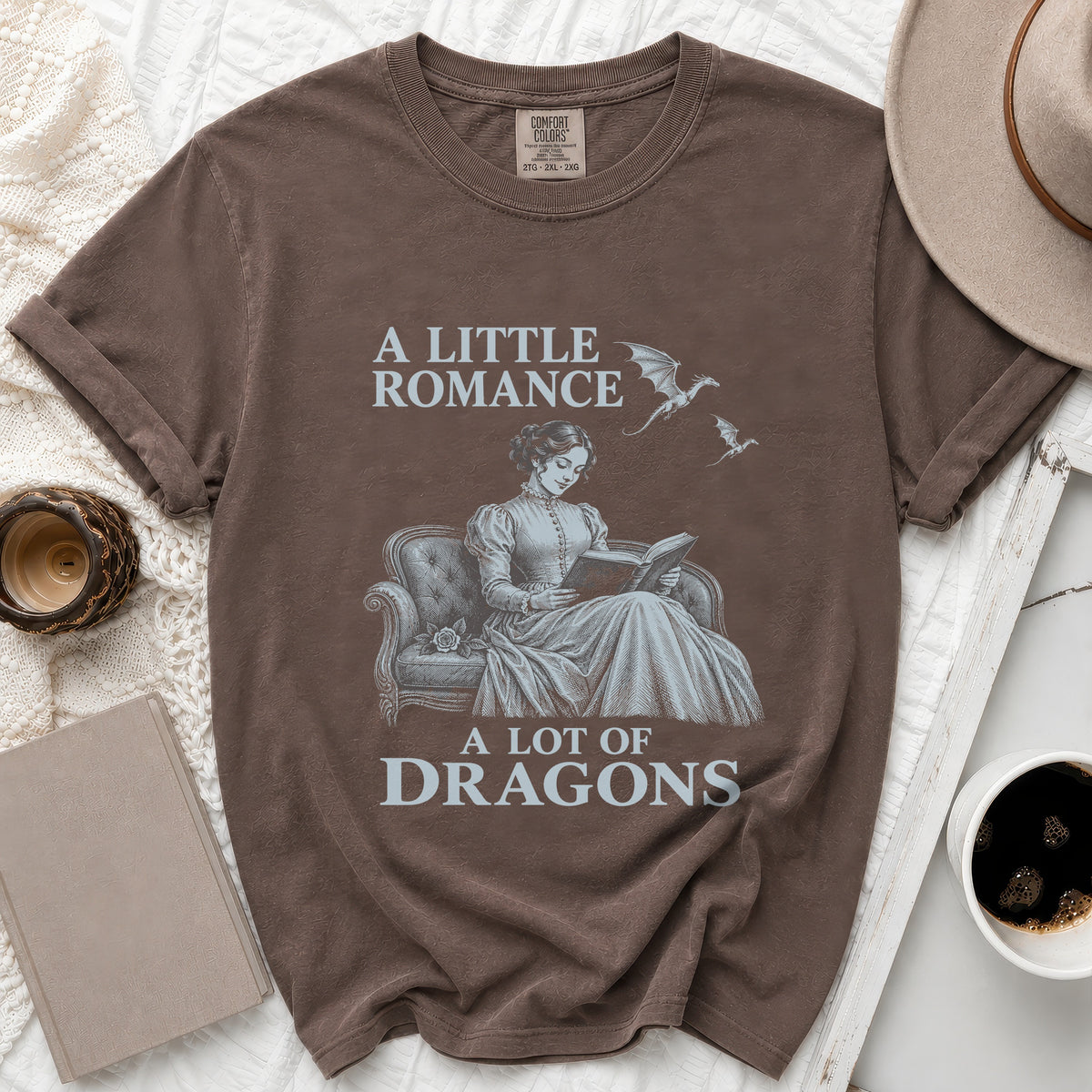 Brown t-shirt with graphic: "A Little Romance A Lot of Dragons" with woman reading and dragons.