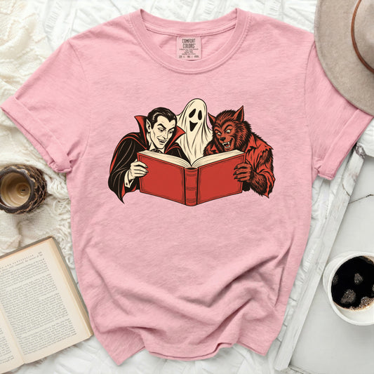 Dracula, ghost, and werewolf reading a book together on a pink t-shirt.