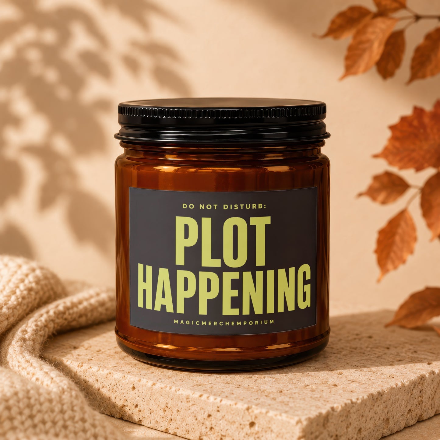 Brown glass candle with black lid, featuring a dark label with yellow text "DO NOT DISTURB: PLOT HAPPENING".