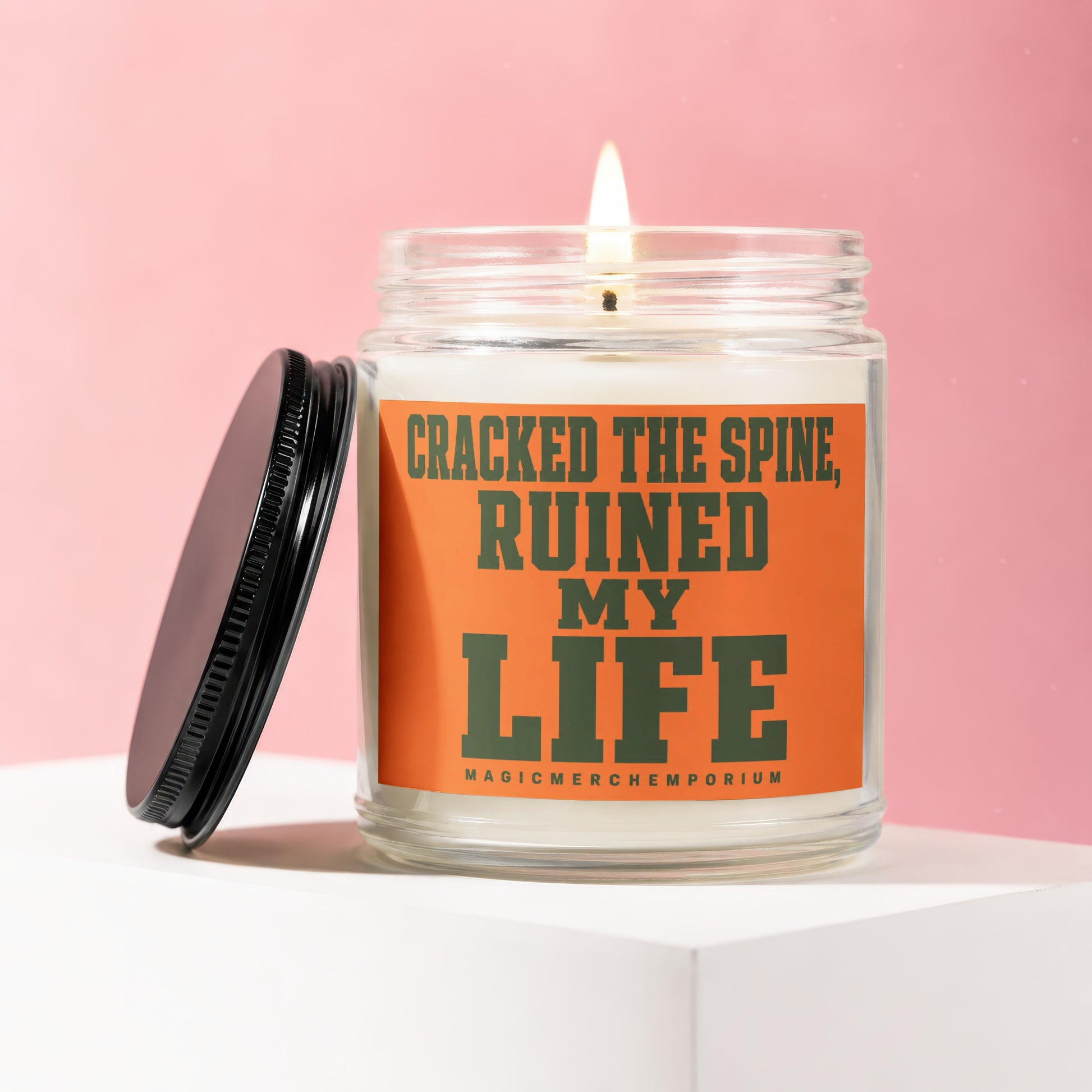 Candle with orange label saying "CRACKED THE SPINE, RUINED MY LIFE"