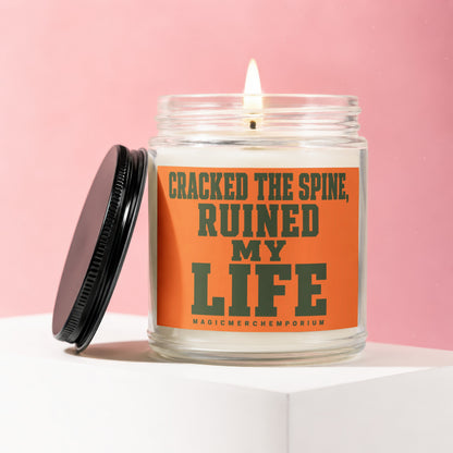 Candle with orange label saying "CRACKED THE SPINE, RUINED MY LIFE"