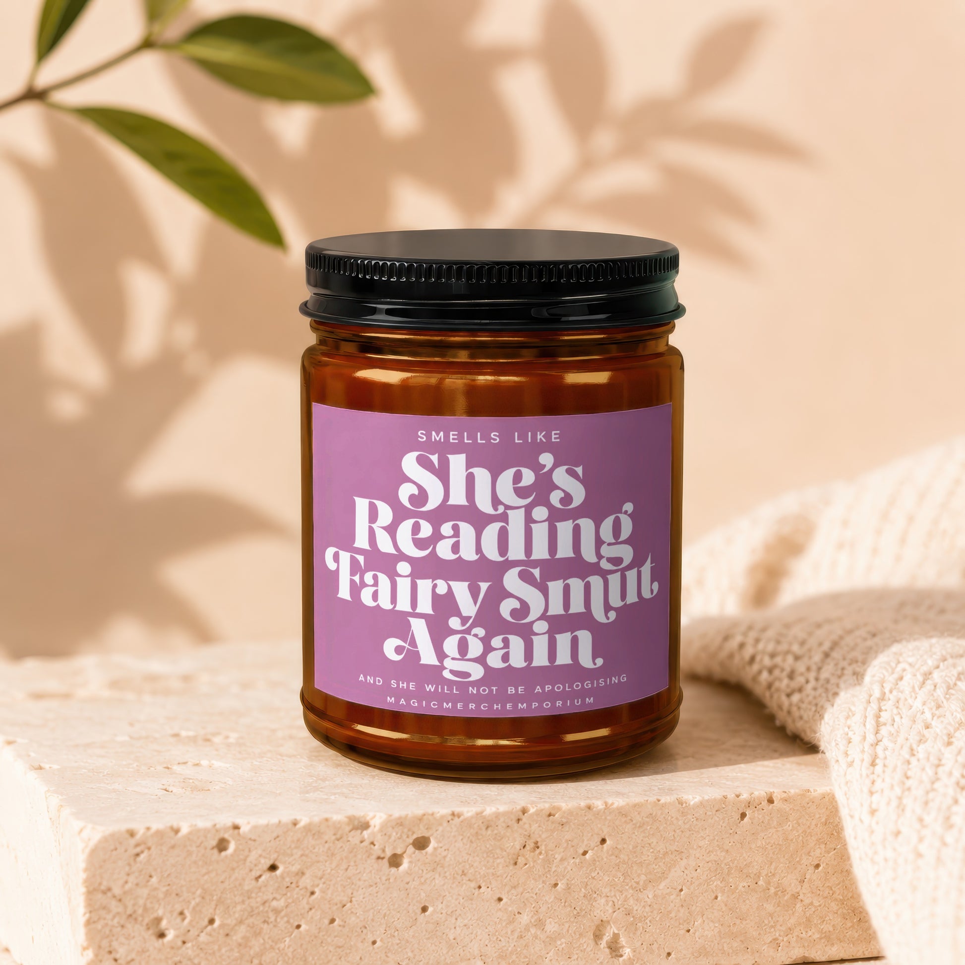 Amber jar candle with purple label reading "Smells Like She's Reading Fairy Smut Again".