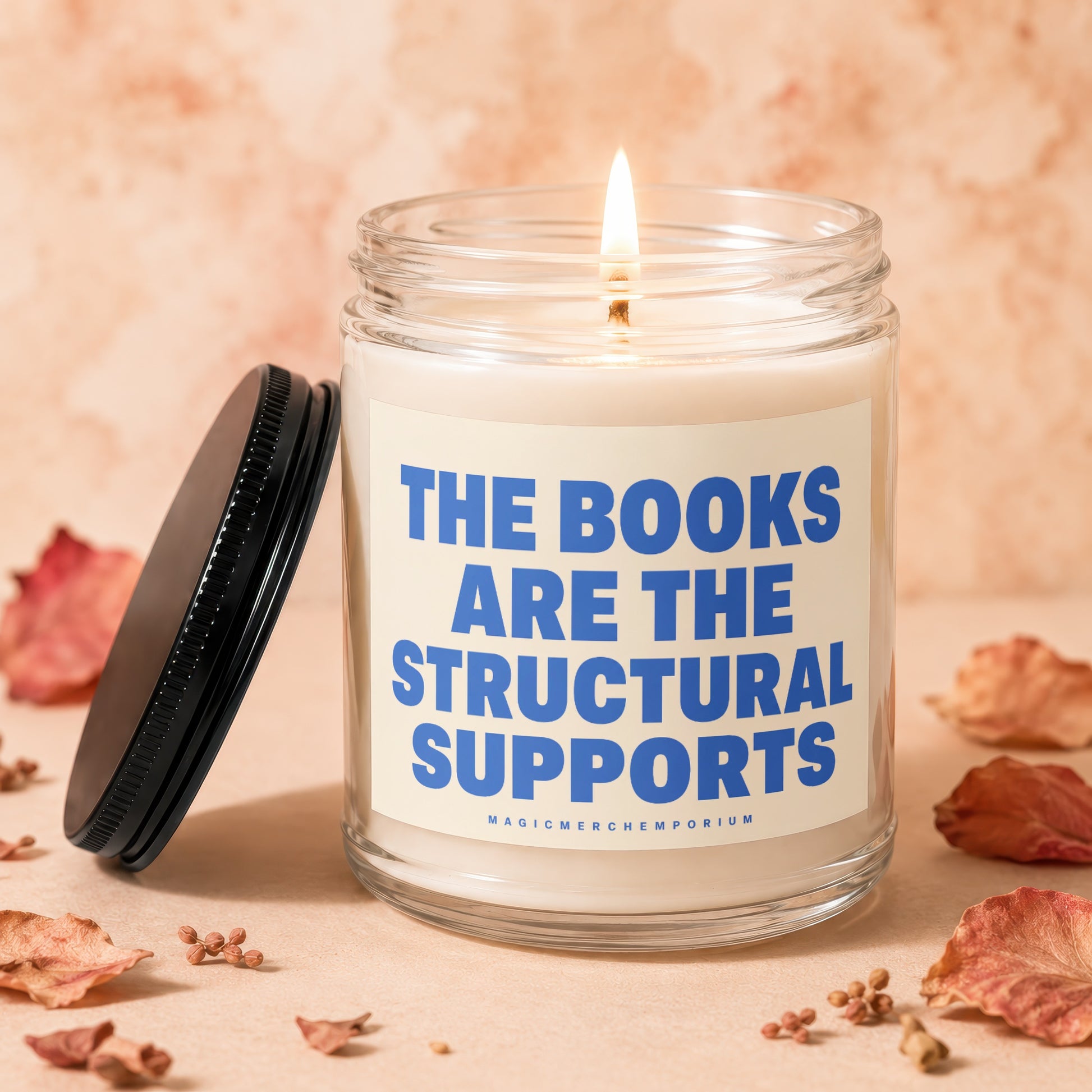 Glass candle with lit wick and text "THE BOOKS ARE THE STRUCTURAL SUPPORTS."