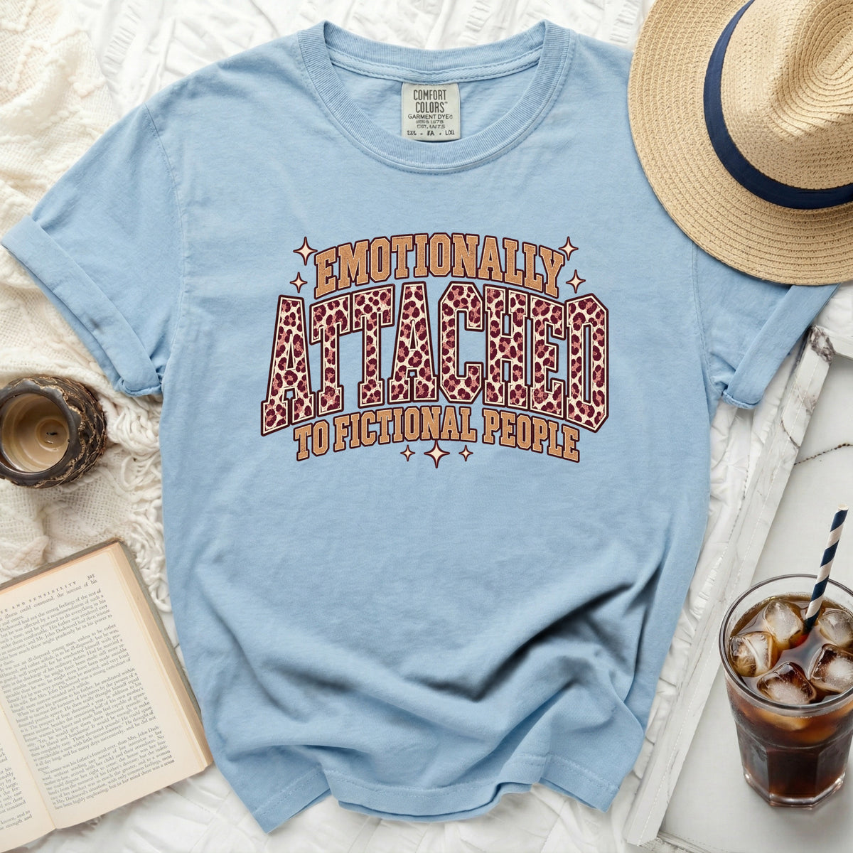 Light blue t-shirt with "Emotionally Attached To Fictional People" leopard print graphic.