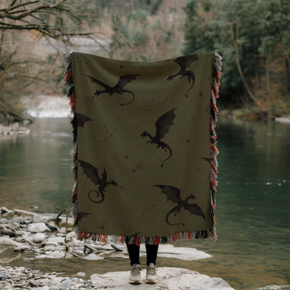 A person is standing on a rock, holding a large blanket with a dragon design on it, partially covering their face.