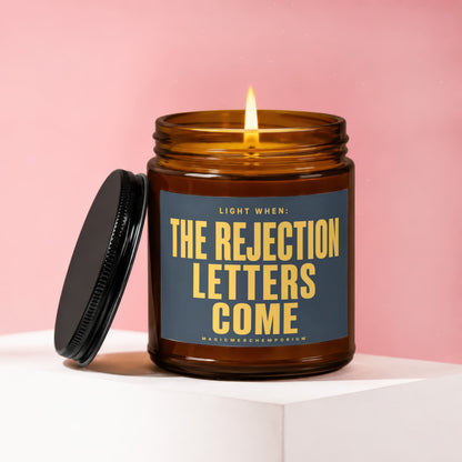 Amber jar candle with lit flame and black lid, reading "Light When: The Rejection Letters Come".