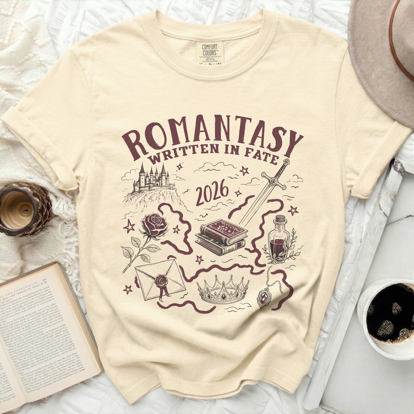 Cream comfort colors t-shirt with romantasya design featuring castle, sword, books, rose, crown, and potion.