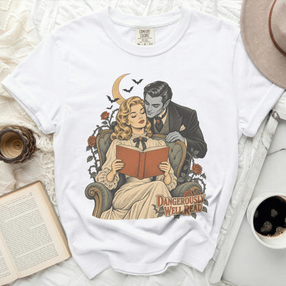 White t-shirt with a graphic of a couple, a moon, bats, and roses with text "DANGEROUSLY WELL READ".