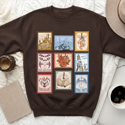 Brown sweatshirt featuring nine fantasy-themed stamps: Lunathion castle, Night Court mountains, sword, bats, roses, art supplies, stag, book with sword, and dragon.