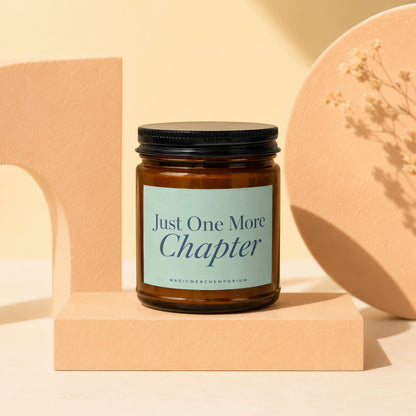 Amber jar candle with black lid and light blue label reading "Just One More Chapter".