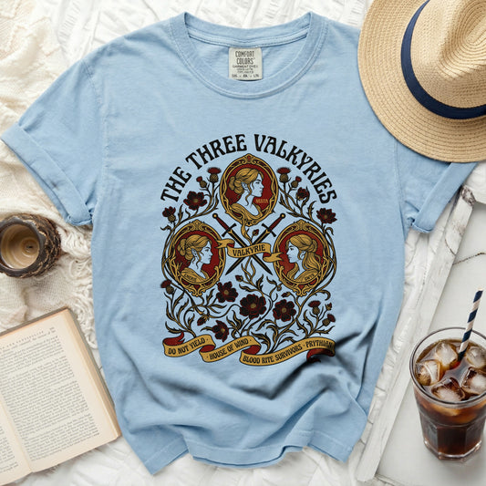 The Three Valkyries graphic on a light blue t-shirt with swords and floral motifs.