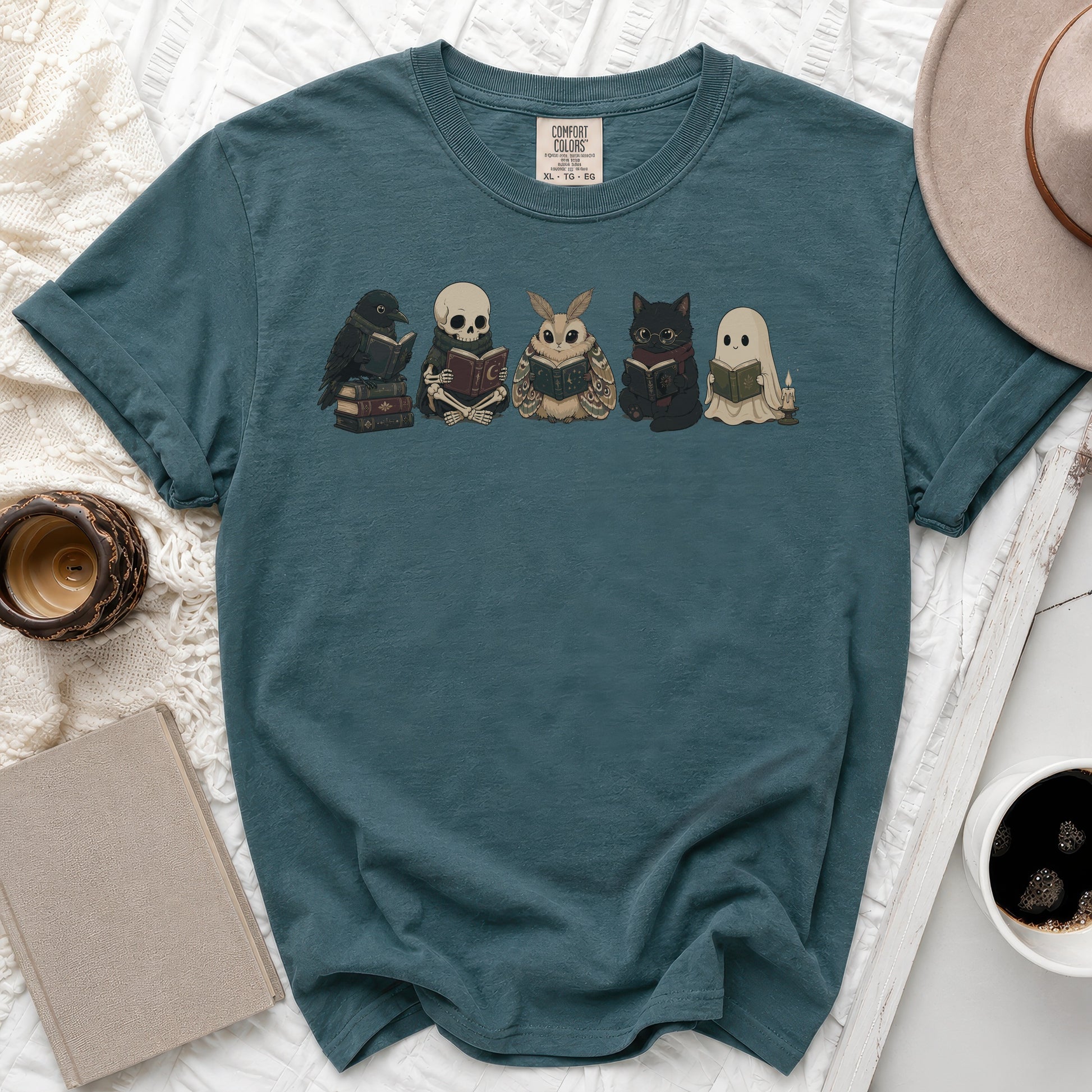 Teal t-shirt with a print of a crow, skeleton, moth, cat, and ghost reading books.