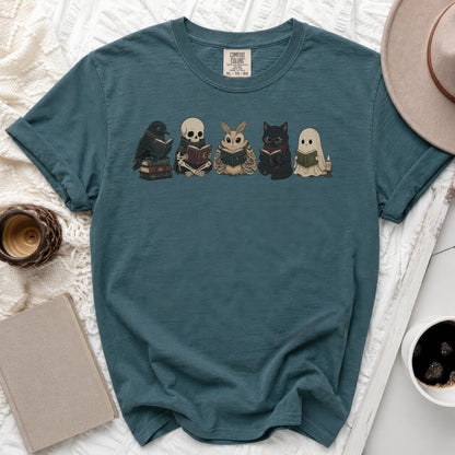 Teal t-shirt with a print of a crow, skeleton, moth, cat, and ghost reading books.