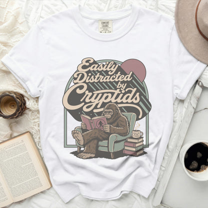 White t-shirt with graphic of Bigfoot reading "Easily Distracted by Cryptids."