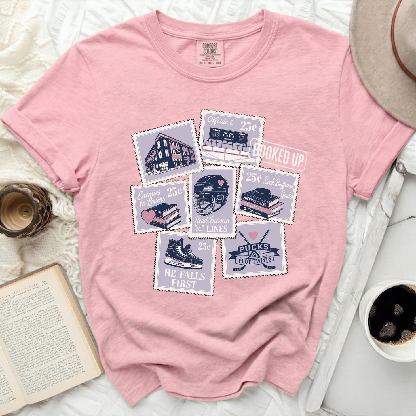 Pink graphic tee with postage stamps featuring book and hockey themes.