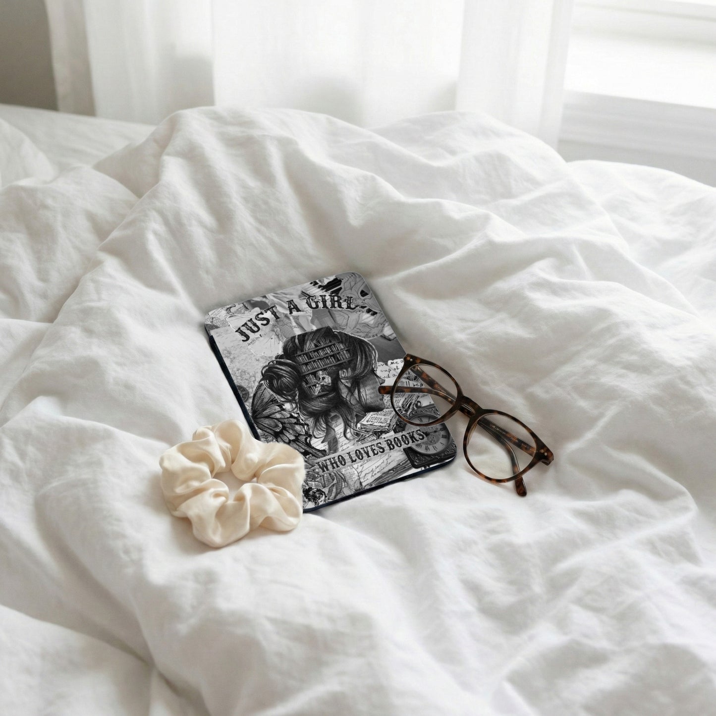 E-reader with "Just a Girl Who Loves Books" text, glasses, and scrunchie on white bedding.