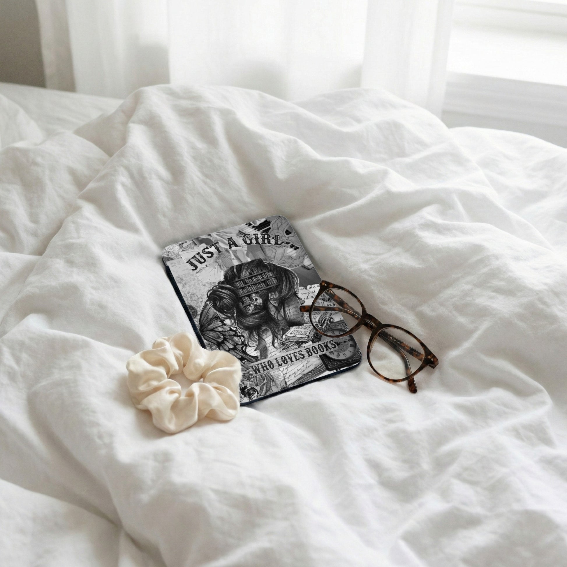 E-reader with "Just a Girl Who Loves Books" text, glasses, and scrunchie on white bedding.