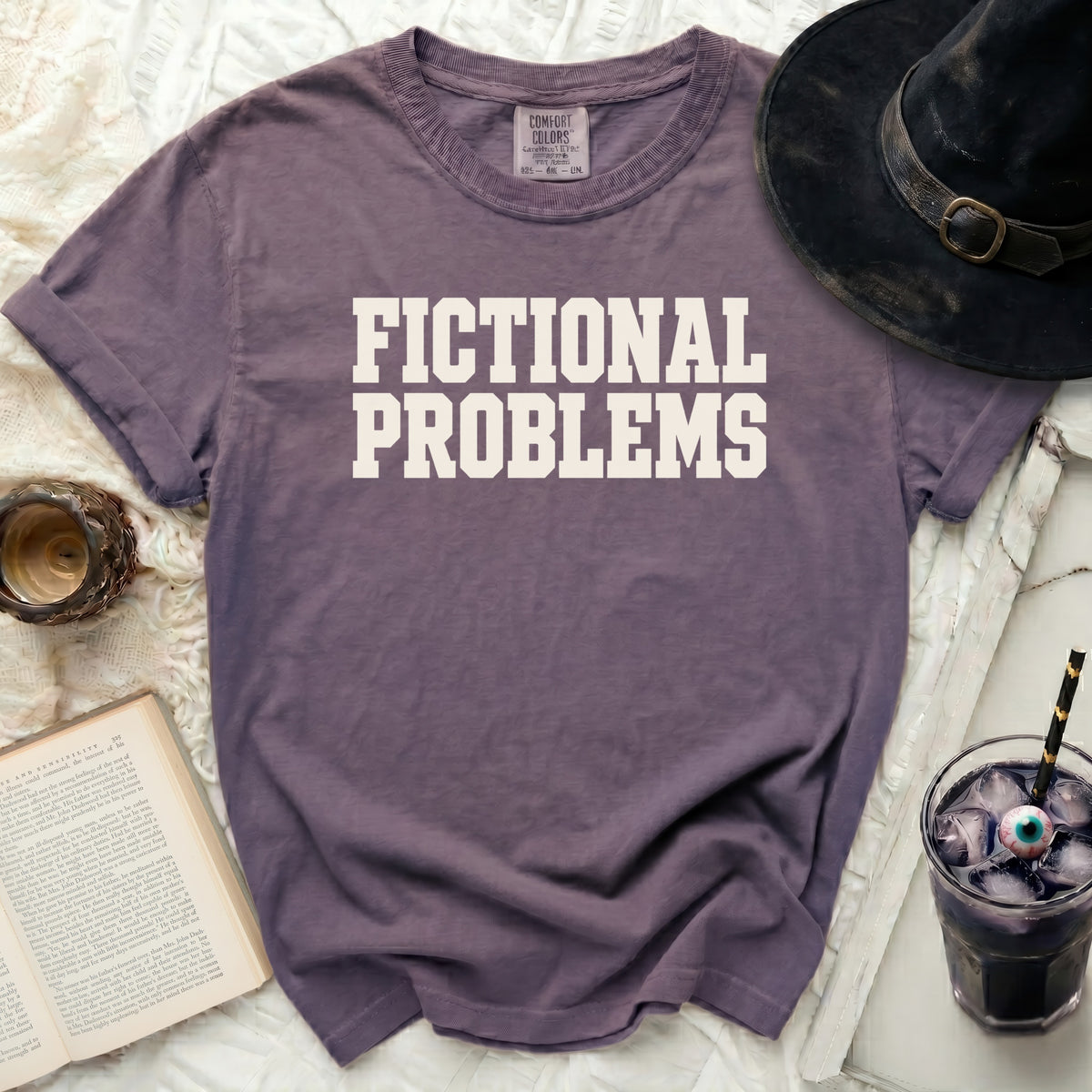 Purple t-shirt with white text "FICTIONAL PROBLEMS" and a witch hat.