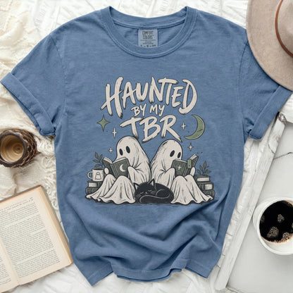Blue t-shirt graphic with text "HAUNTED BY MY TBR", two ghosts reading, and a sleeping cat.