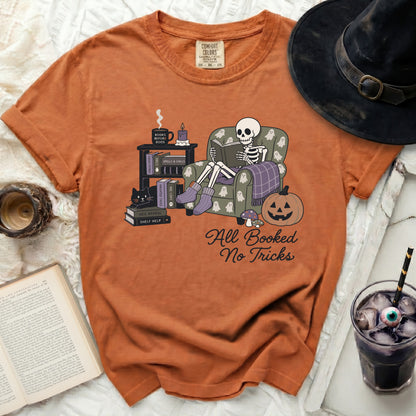 Skeleton in armchair reading, text "All Booked No Tricks", with Halloween elements.