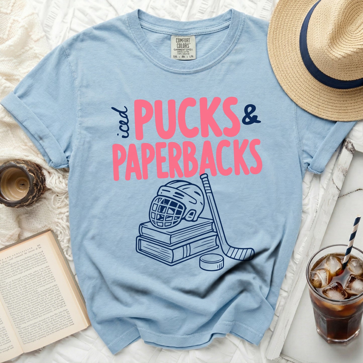Light blue t-shirt with "Pucks & Paperbacks" text and hockey graphics.