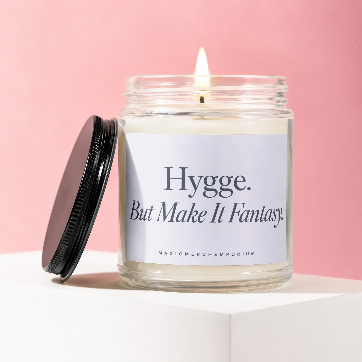 Lit candle in glass jar with black lid, text reads "Hygge. But Make It Fantasy."