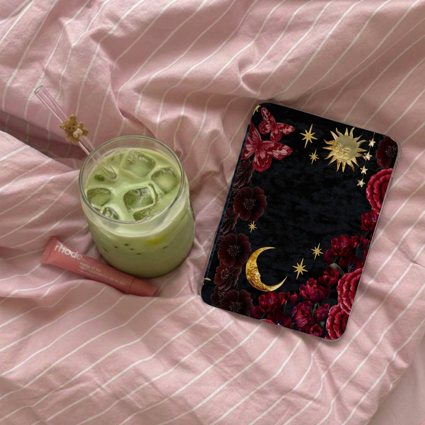 Black phone case with celestial and floral design next to matcha drink and lip balm.