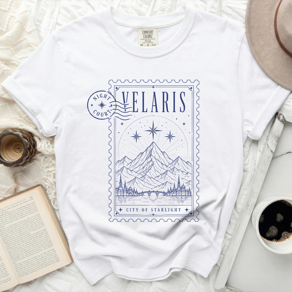 White t-shirt with blue graphic of mountains, city, and stars in a stamp design.