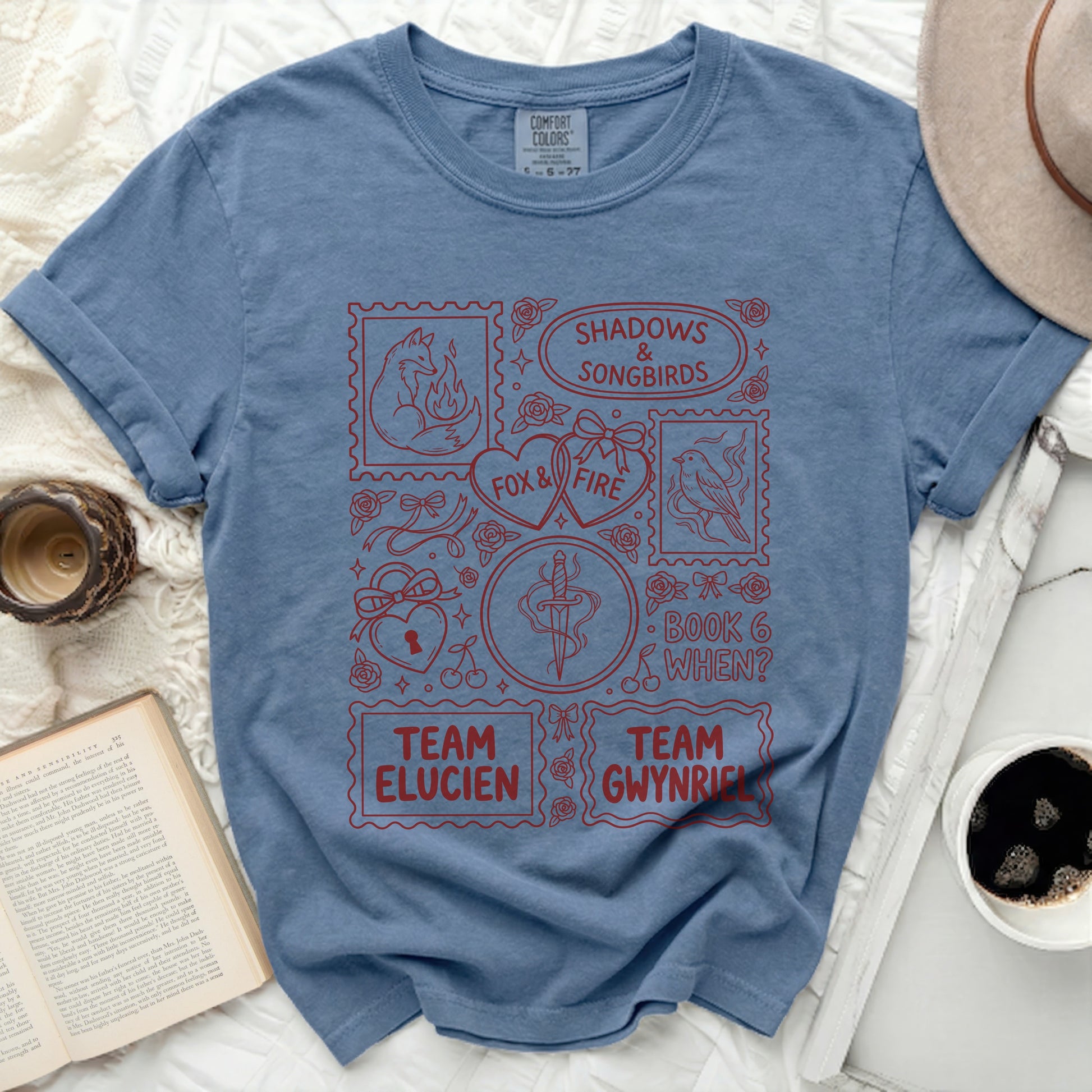 Blue t-shirt with red graphic art of foxes, birds, swords, hearts, and text.
